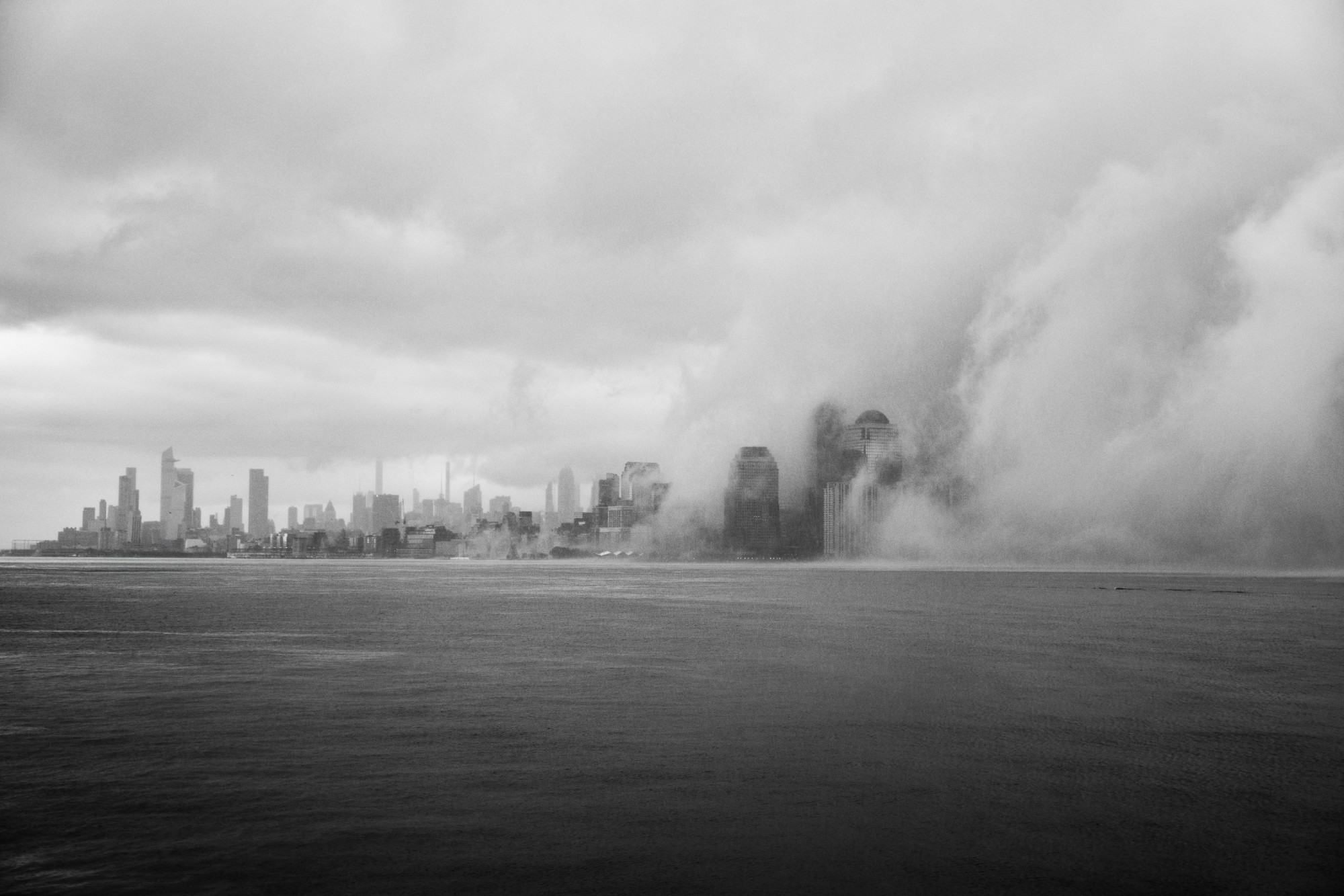 « Smoke on the city » : des gratte-ciel émergent d'un épais banc de brouillard au-dessus de l'eau, en noir et blanc